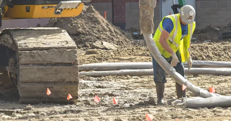 Construction worker laying pipes at a site.