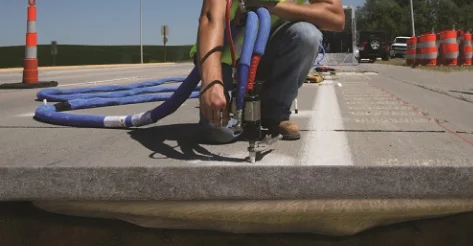 Worker installing cables on road curb.