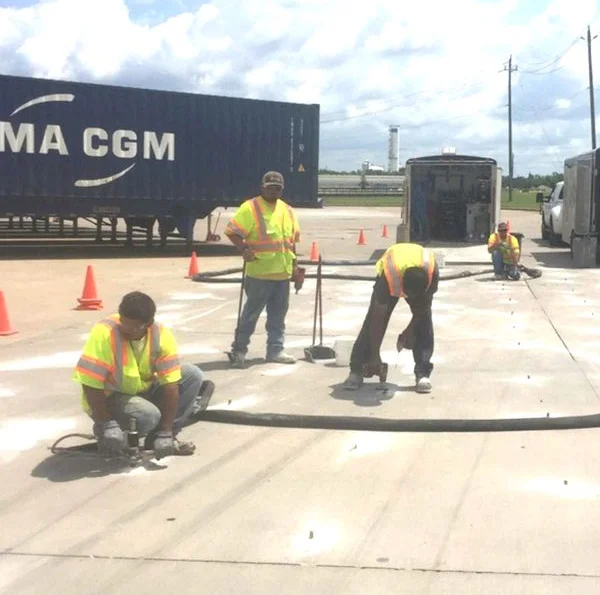 Workers in hi-vis repairing pavement at industrial site.