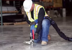 Construction worker using a tool on concrete floor.