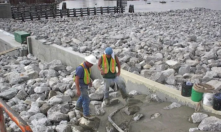 Workers laying concrete near a rock-filled construction site.