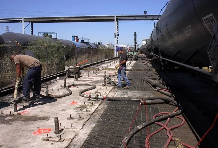 Workers maintaining railroad tank cars at industrial site.