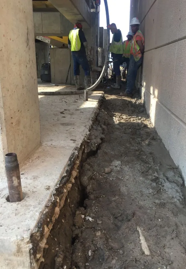 Workers pour concrete in construction trench.