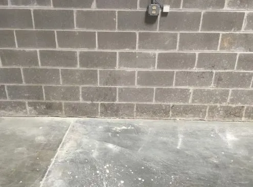 Gray brick wall with electrical outlet and concrete floor.