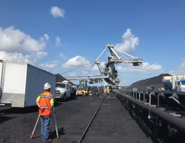 Workers near coal conveyor and crane on sunny day.