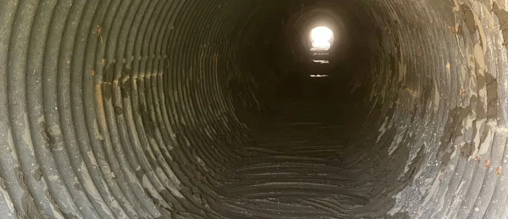 Corrugated metal tunnel with light at the end.