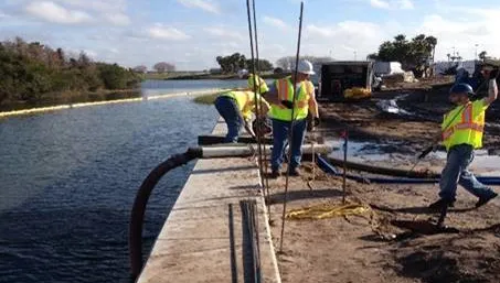 Workers managing hoses by waterway.