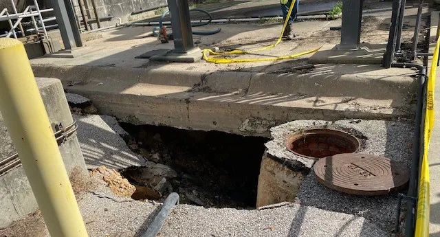 Industrial site sinkhole near manhole and safety barriers.