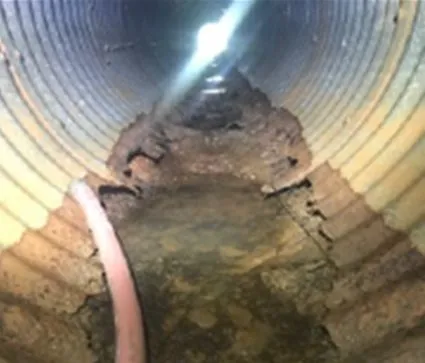 Damaged underground pipe interior with debris.