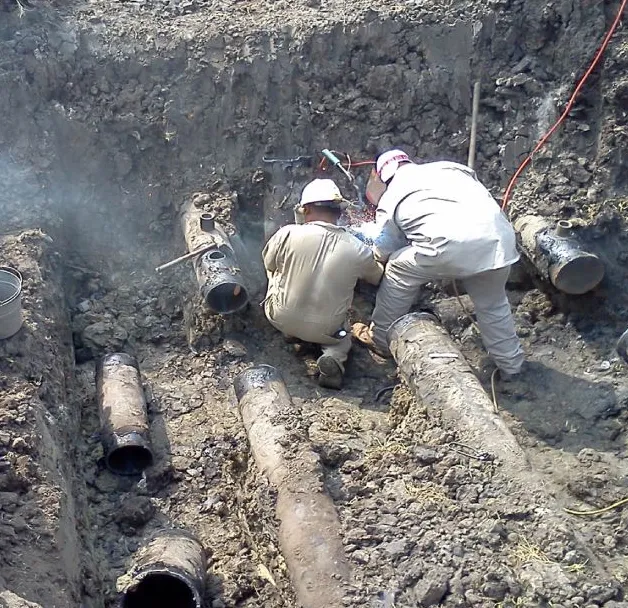 Workers repairing underground pipes in trench.