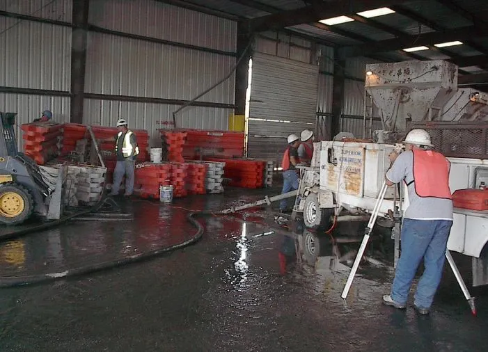 Workers cleaning warehouse floor near forklift and concrete mixer.