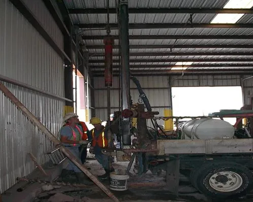 Workers operating drilling equipment indoors.