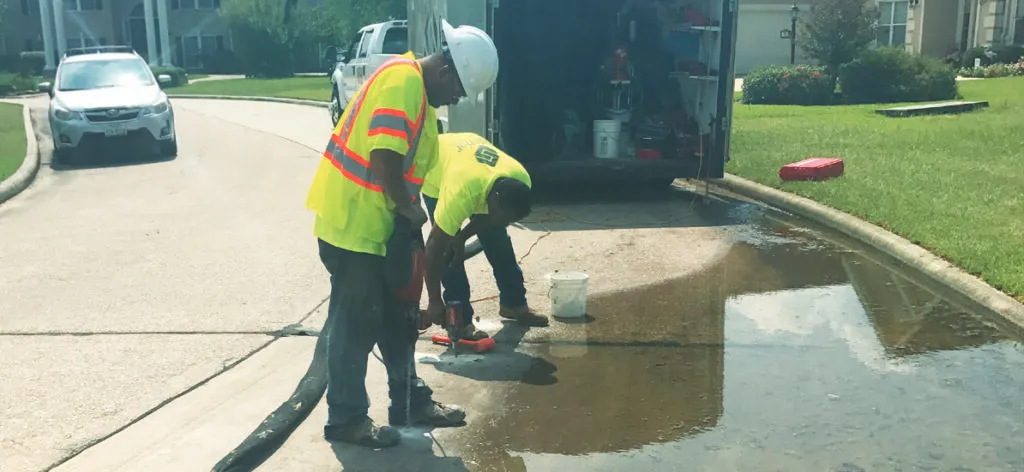 Workers inspecting water leakage on residential street.