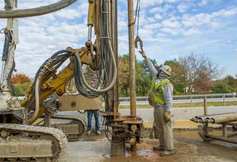 Workers operating heavy drilling machinery outdoors.