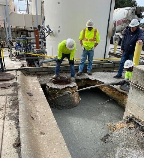 Workers inspecting manhole at industrial site.