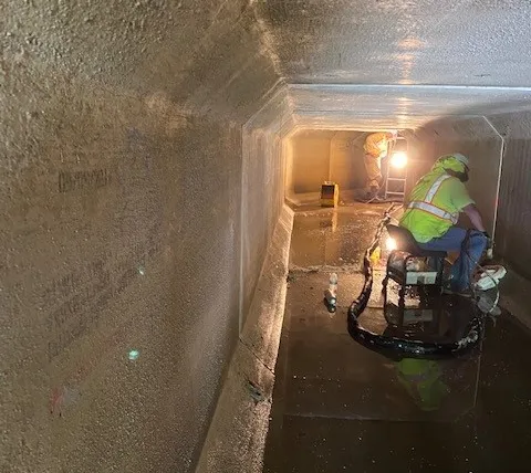 Worker inspects water-filled underground tunnel.