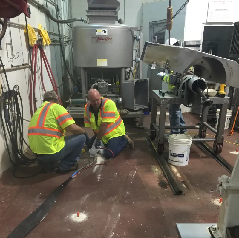 Workers in high-visibility vests repairing industrial machinery.