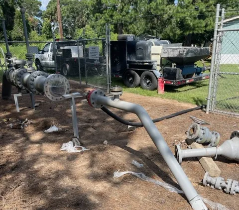 Industrial equipment and piping outdoors near fence.