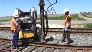Workers operating machinery on railroad tracks.