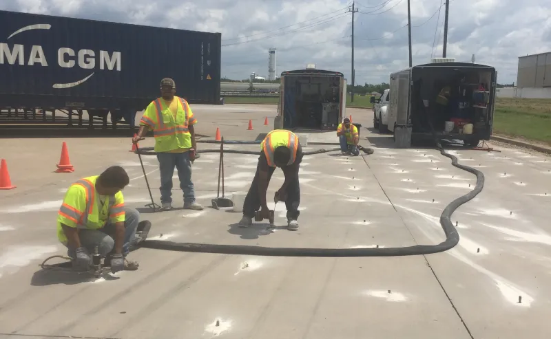 Workers applying sealant on concrete near trucks.