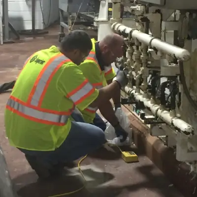 Workers repairing machinery in industrial setting.