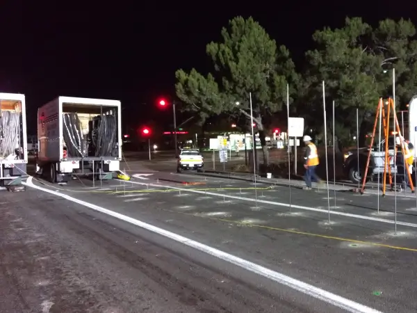Nighttime roadwork with workers, vehicles, and traffic lights.